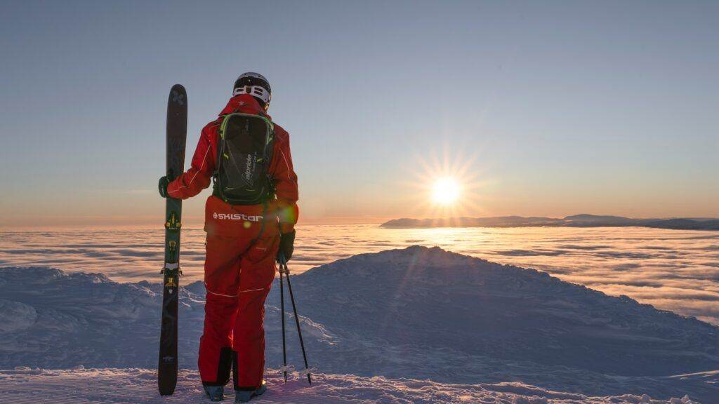 a man holding skis standing on top of a snow covered slope