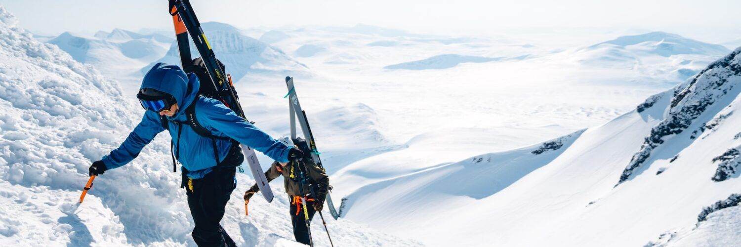 a man walking up a snow covered mountain holding skis