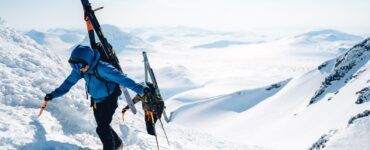 a man walking up a snow covered mountain holding skis