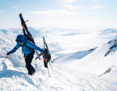 a man walking up a snow covered mountain holding skis