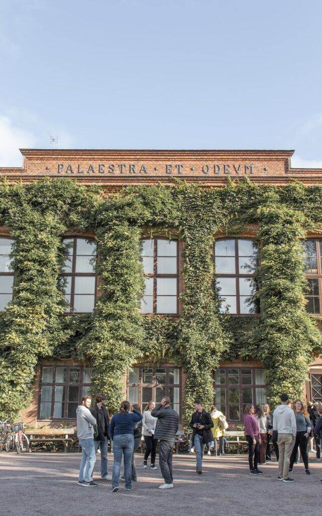 a group of people standing outside a building with ivy on it