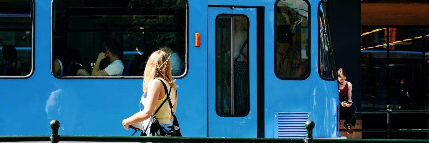 woman in black leather backpack standing beside blue and white train during daytime