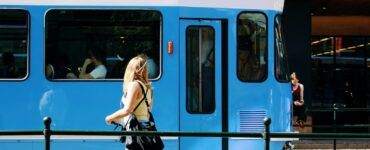 woman in black leather backpack standing beside blue and white train during daytime