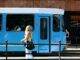 woman in black leather backpack standing beside blue and white train during daytime