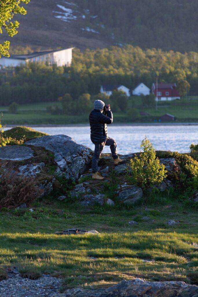 man in black jacket and black pants standing on rock near body of water during daytime